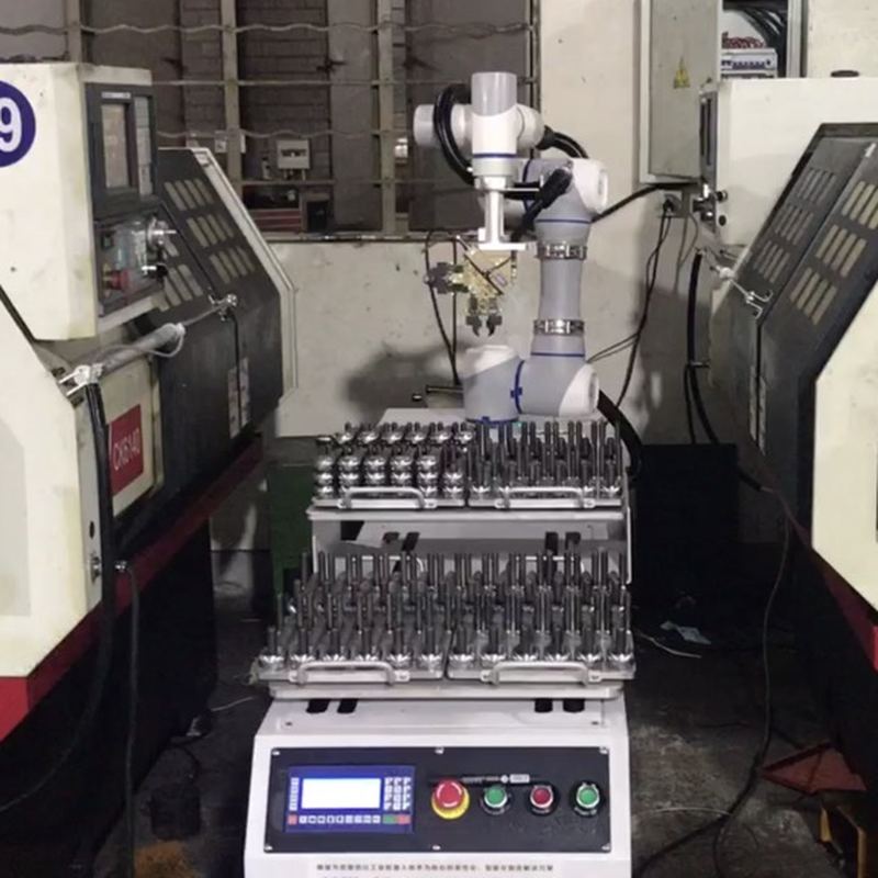 A cobot between two CNC lathes, with a workpiece carrier of turned parts in front of it.