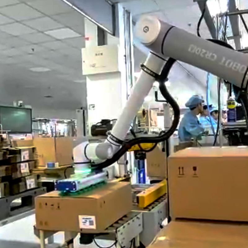 A DOBOT CR20A cobot placing a carton from the conveyor onto a pallet, with a finished pallet stack alongside it on a factory floor.