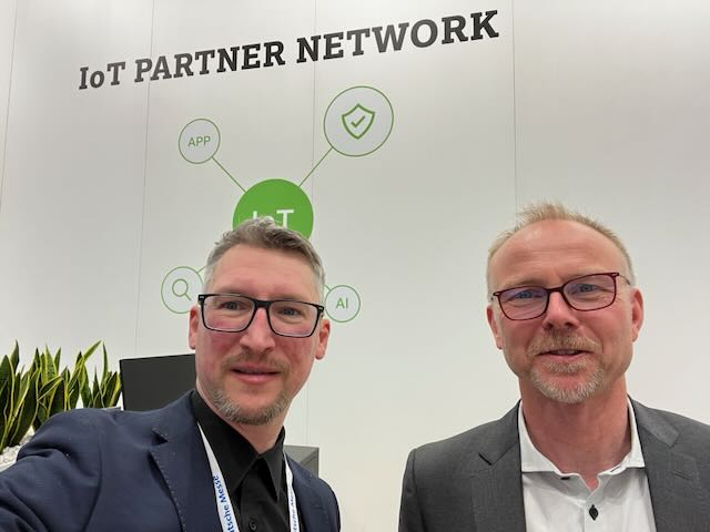 Zwei Personen mit Deutsche-Messe-Ausweis vor dem IoT-Partner-Network-Aufsteller auf der Hannover Messe 2023.