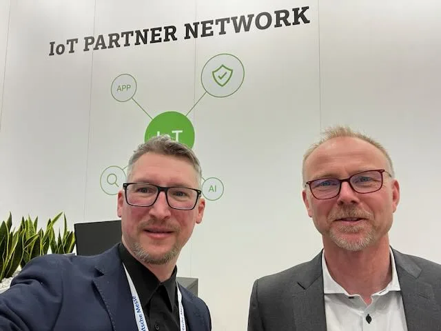 Two people with Deutsche Messe badges in front of the IoT Partner Network display at Hannover Messe 2023.