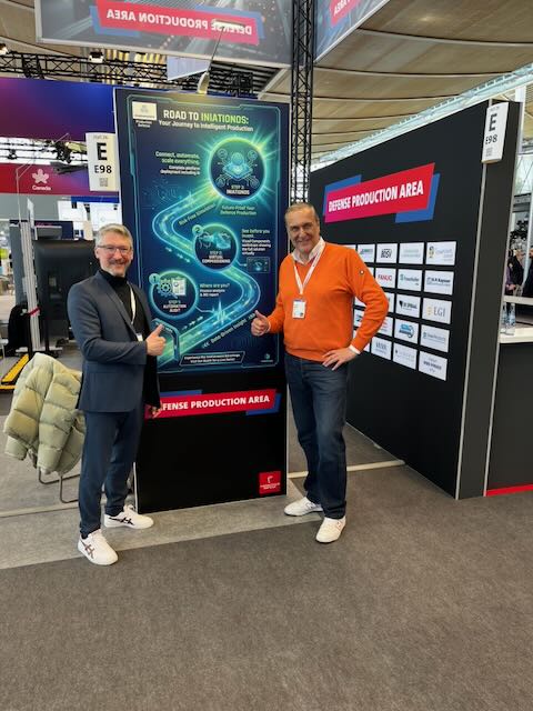 Zwei Personen vor dem Road-to-iniationOS-Aufsteller im Defense Production Area auf der Hannover Messe 2026.