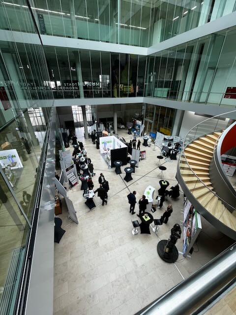 Blick von oben in die Eventhalle des Produktionsforums mit Ständen, Stehtischen und Besuchern.
