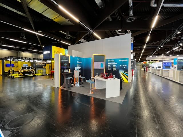 iniationWARE-Messestand auf der SPS Nürnberg 2025 mit dunklen Wandpaneelen, orangefarbenen Lichtleisten und Tresen mit Demotechnik.
